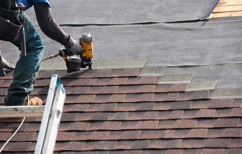 A worker installing shingles on a roof using a nail gun. | Holbrook Leavitt & Associates PLLC
